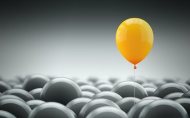 Different, unique and standing out of the crowd concept. An orange baloon is different and above the other gray ones, representing the individuality in the masses.