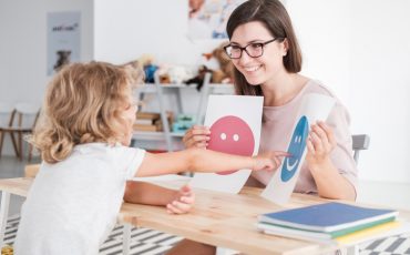 Smiling counselor holding pictures during meeting with young patient with autism